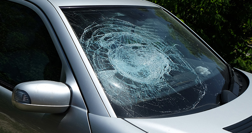  Front view of a silver car with extensive circular cracks across the windscreen